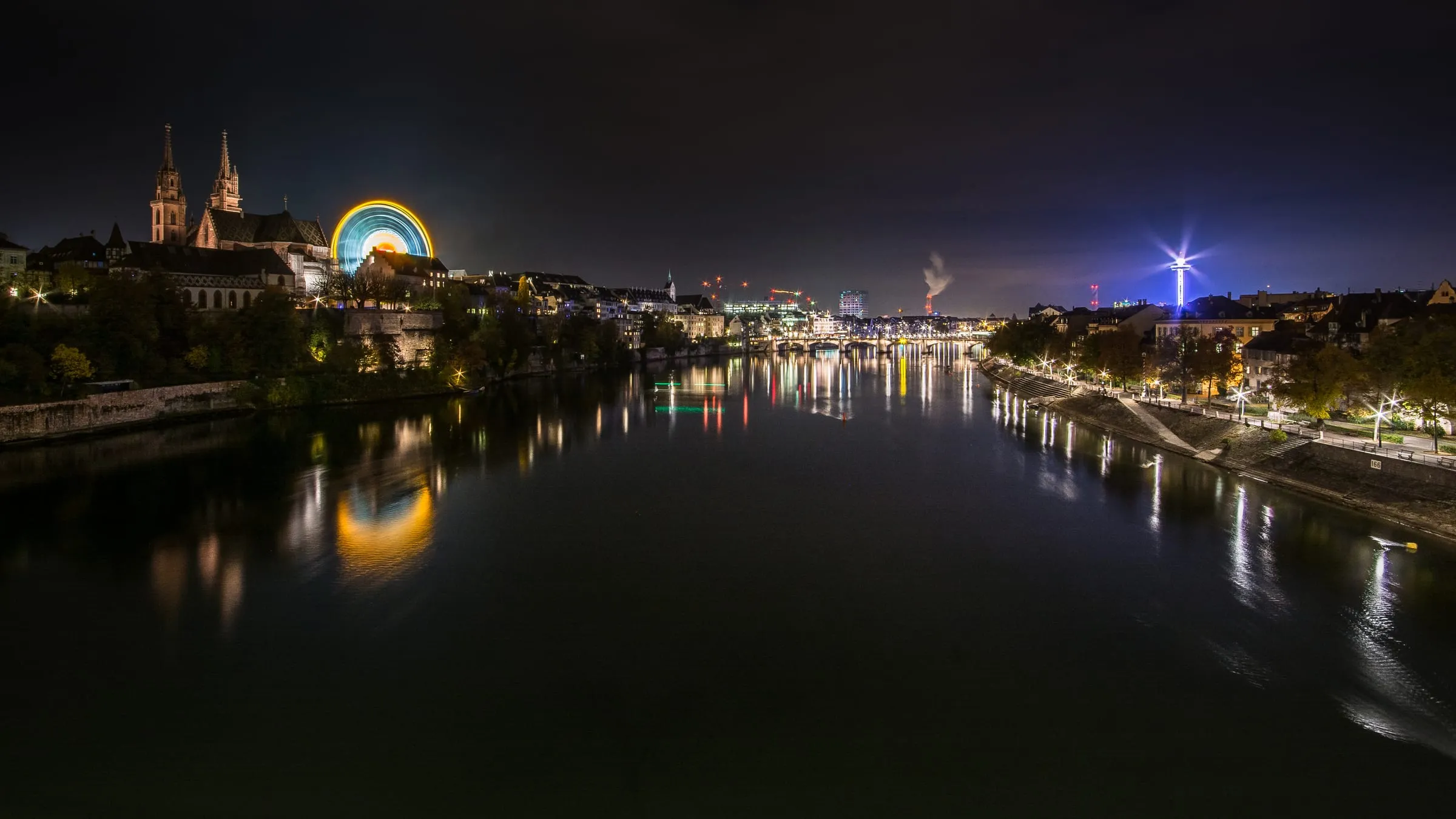 Panorama der Basler Herbstmesse bei Dämmerung mit beleuchtetem Riesenrad und Fahrgeschäften
